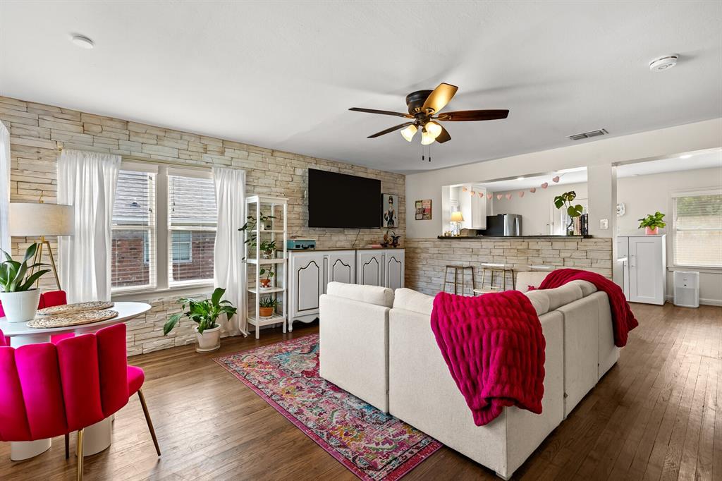 Living area featuring stacked stone accent wall, wood-finish flooring, ceiling fan, and pass-through opening