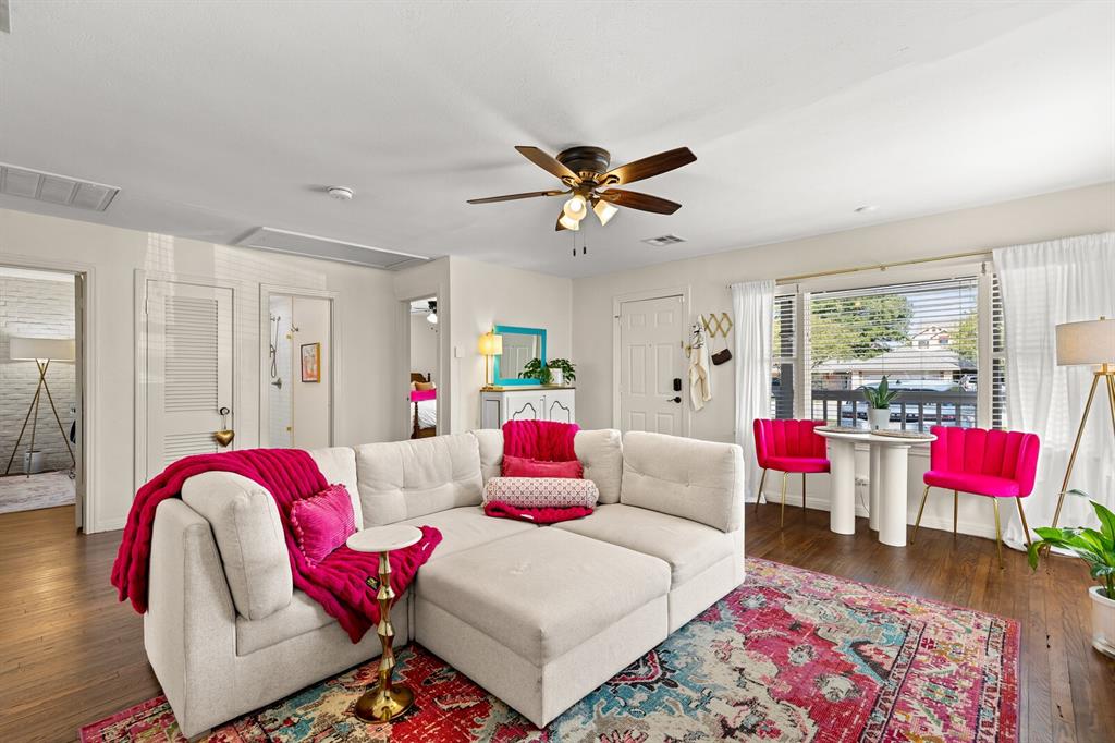 Living space featuring wood-finish flooring, a ceiling fan with integrated lighting, and a large window with blinds