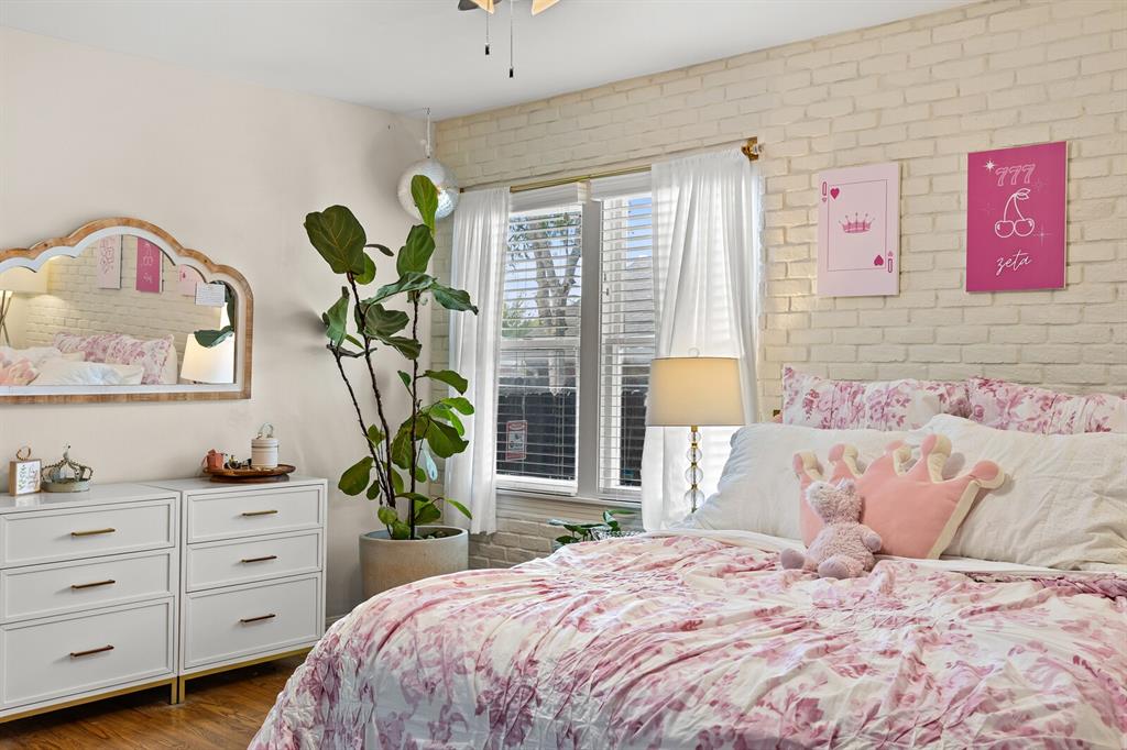 Interior space featuring a painted brick accent wall, double-hung windows with horizontal blinds, and wood-finish flooring