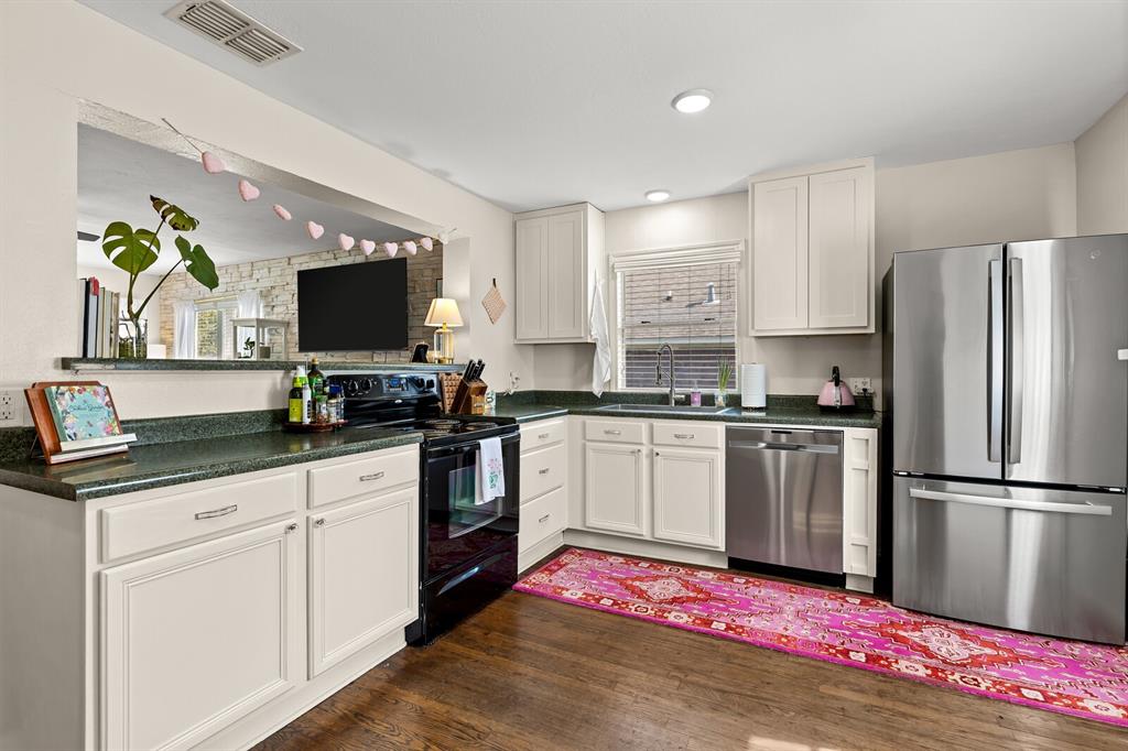 Kitchen featuring white cabinetry, solid-surface countertops, recessed lighting, and stainless steel appliances, including a refrigerator and dishwasher, set against wood-finish flooring
