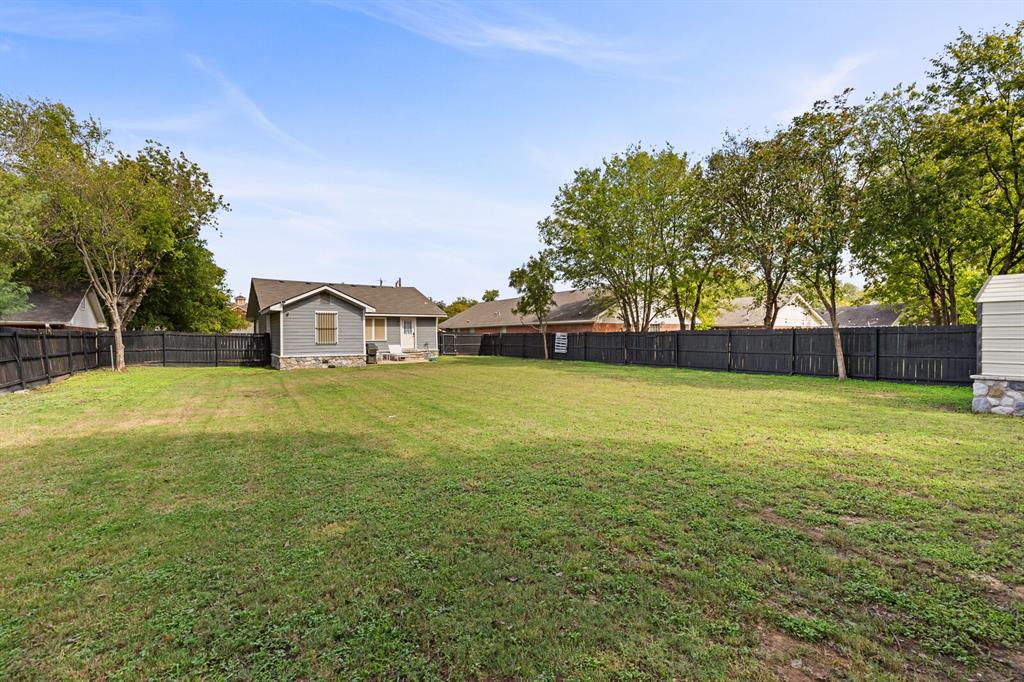 Expansive backyard featuring a large grass lawn, a solid black wood-style privacy fence, and mature trees