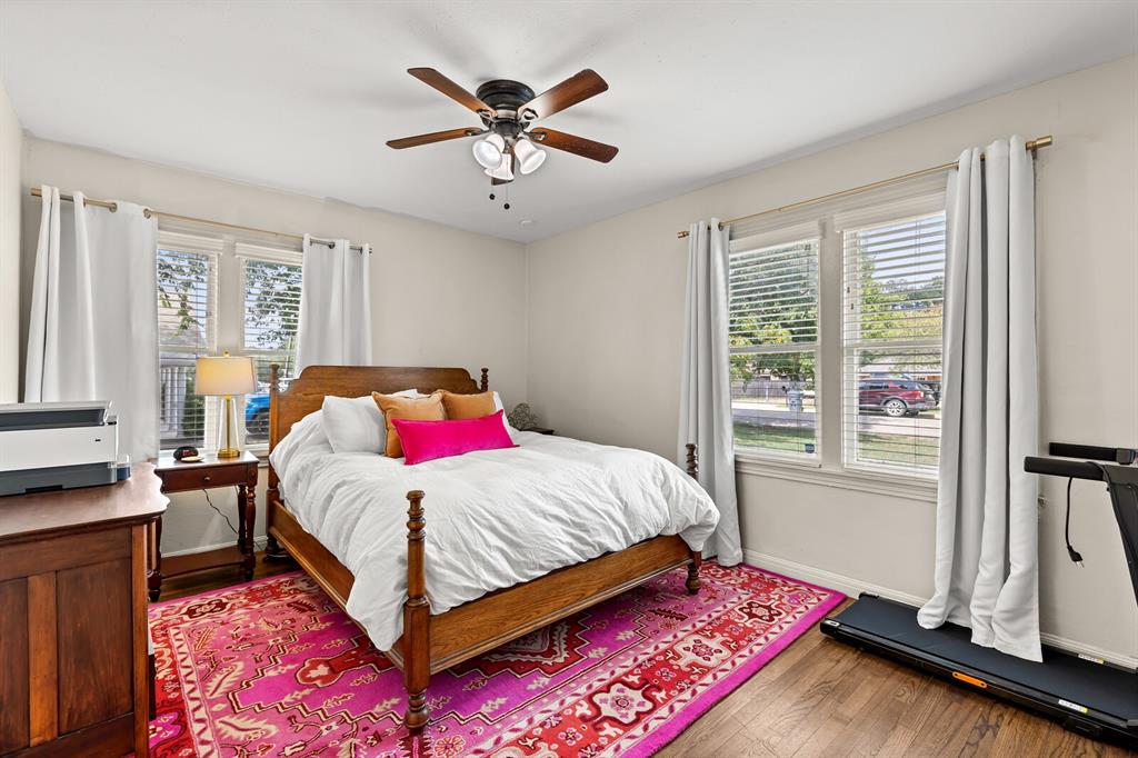 Room featuring wood-finish flooring, dual windows with blinds, and a central ceiling fan with integrated lighting