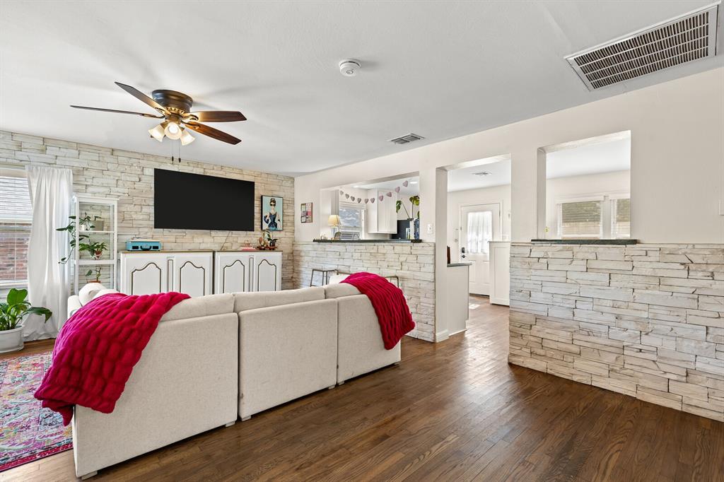 Living area featuring stack-stone accent walls, wood-finish flooring, and a ceiling fan with integrated light fixture