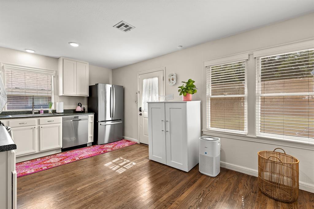 Kitchen featuring stainless steel appliances, white cabinetry, dark stone-finish countertops, wood-finish flooring, and multiple windows