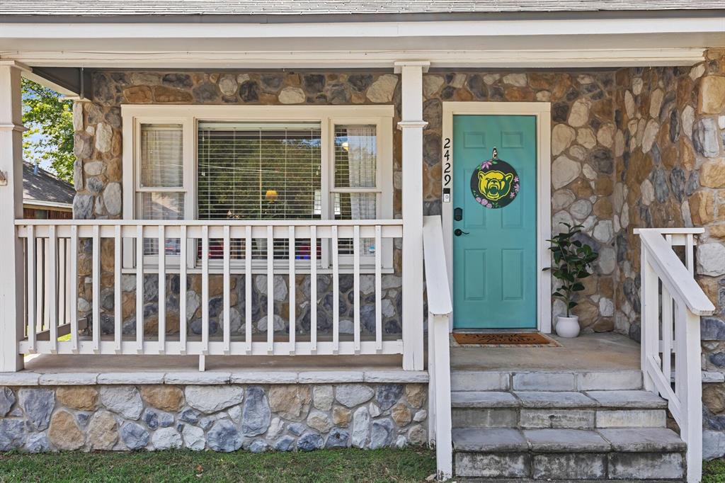 Covered front porch with white railing, natural stone exterior siding, and concrete steps