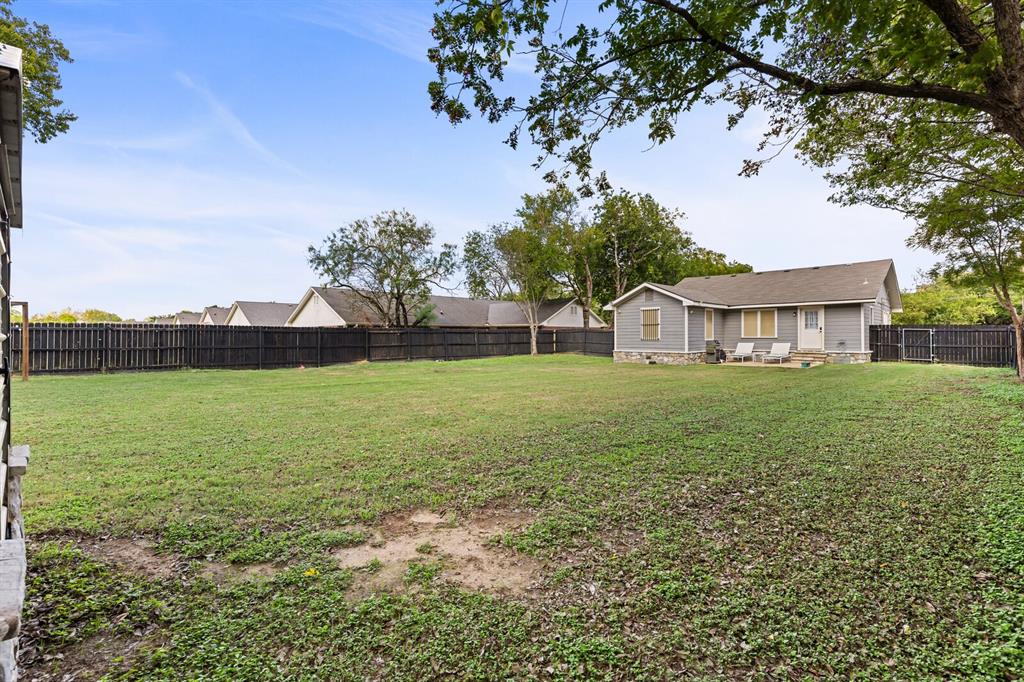 Expansive backyard featuring a large grass lawn, perimeter wood privacy fencing, a stone-accented exterior foundation, and mature trees