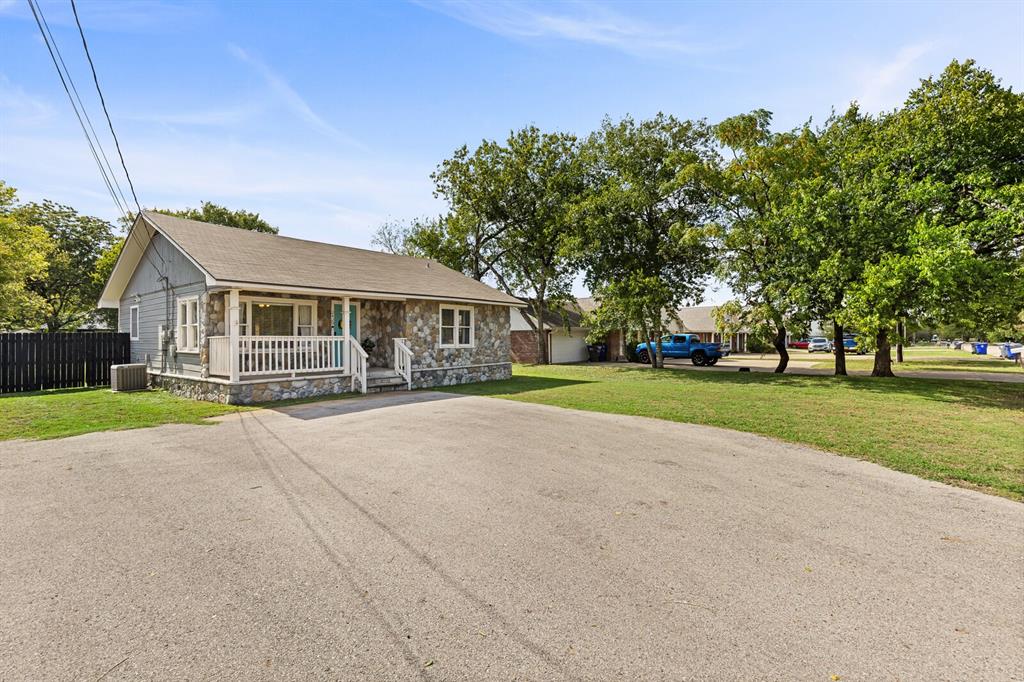 Exterior facade featuring stone veneer siding, horizontal lap siding, a covered front porch with white railing, and an asphalt-paved driveway