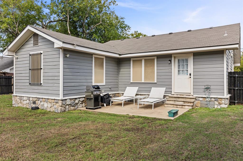 Exterior featuring grey horizontal siding, stone veneer foundation accents, concrete patio, and a privacy fence