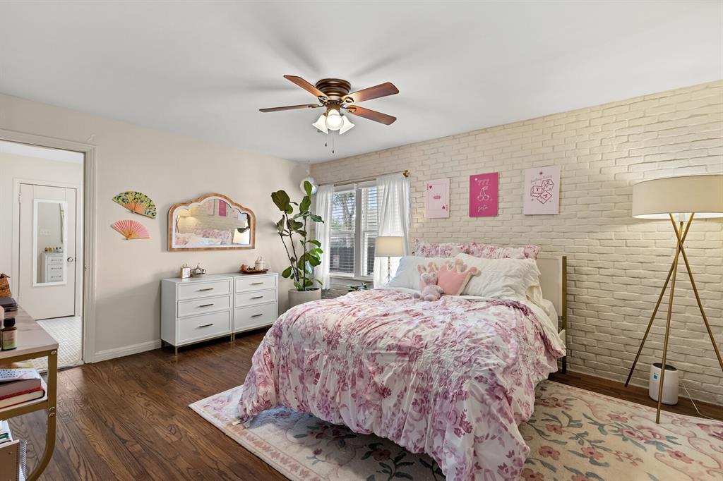 Textured light-toned brick accent wall, wood-finish flooring, and a ceiling fan with integrated lighting