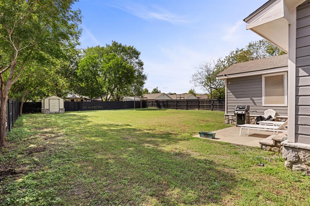 Expansive backyard featuring a concrete patio, perimeter privacy fencing, mature trees, and a detached storage shed