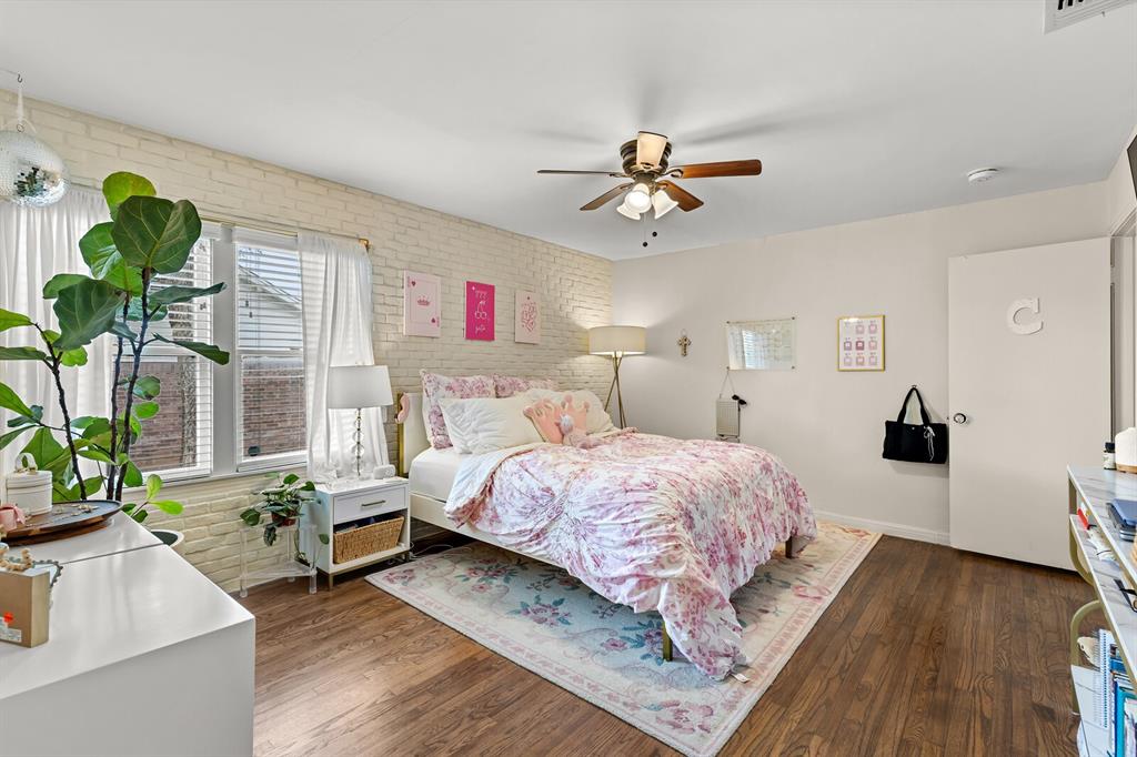 Exposed white brick wall, wood-finish flooring, and a ceiling fan with integrated lighting