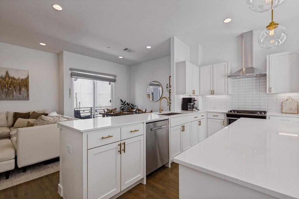 Kitchen featuring white shaker-style cabinetry, quartz countertops, a stainless steel range hood, subway tile backsplash, and wood-finish flooring