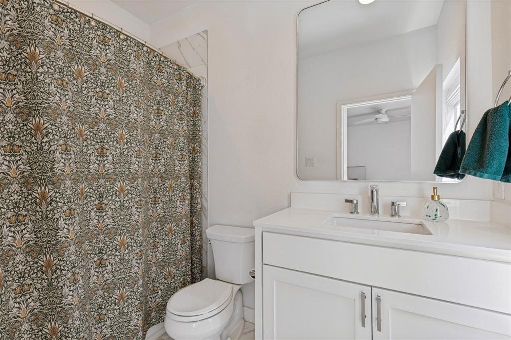 White vanity with a solid surface countertop, rectangular under-mount sink, polished chrome widespread faucet, and a large frameless rounded-corner mirror