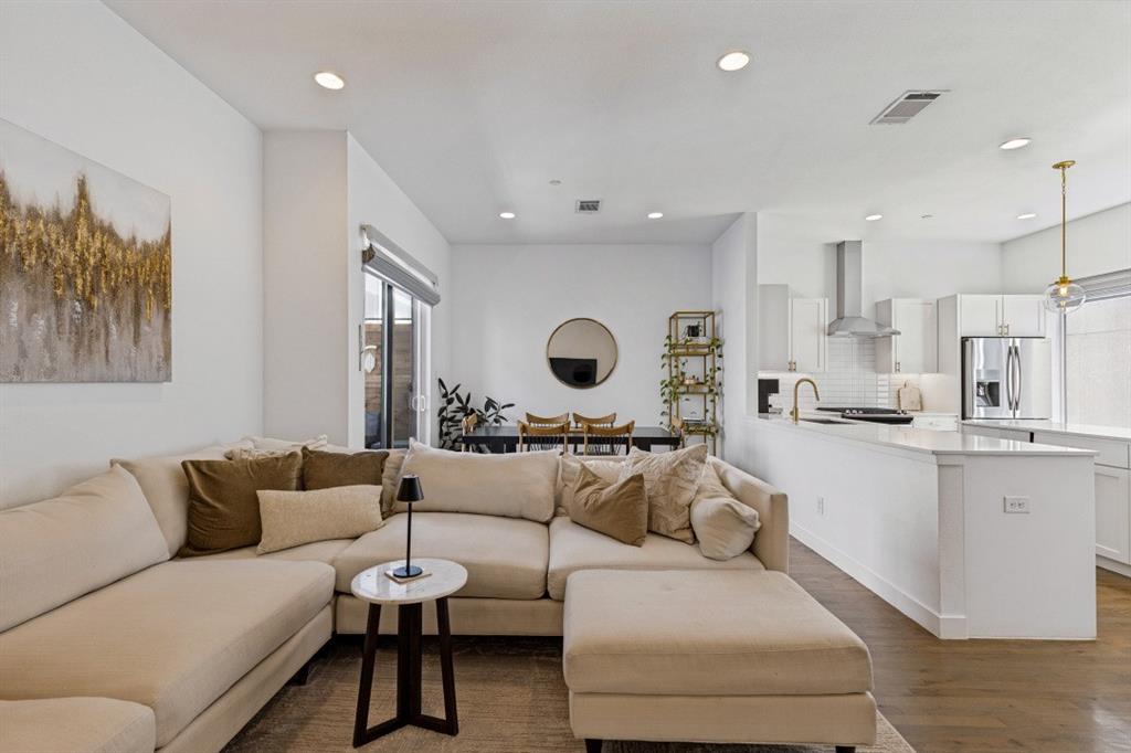 Open-concept living space featuring wood-finish flooring, recessed lighting, white cabinetry, a quartz waterfall-edge peninsula, and a stainless steel range hood