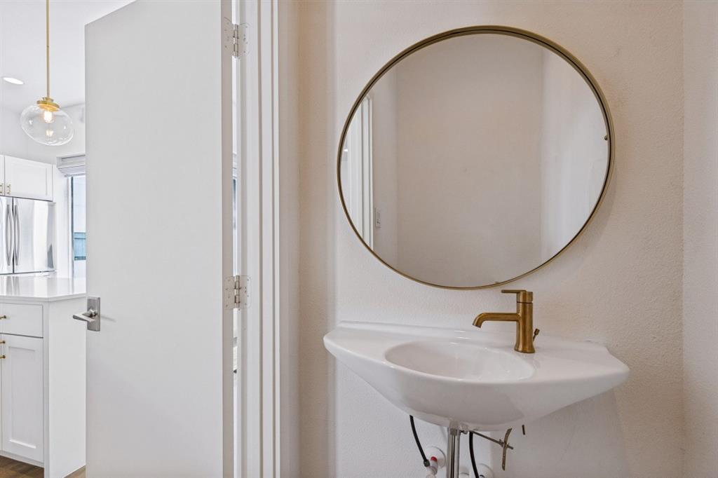 Wall-mounted pedestal sink with a brass-finish faucet, paired with a circular mirror featuring a brass-tone frame