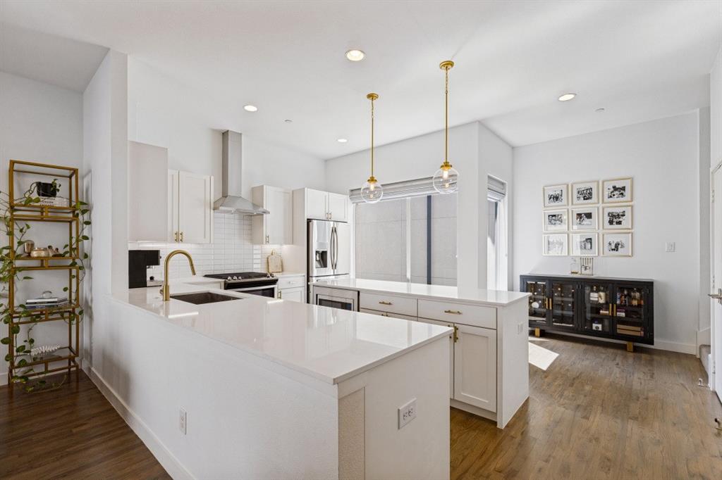 Kitchen featuring white shaker-style cabinetry, quartz countertops, a stainless steel chimney-style range hood, dual glass globe pendant lights, and wood-finish flooring