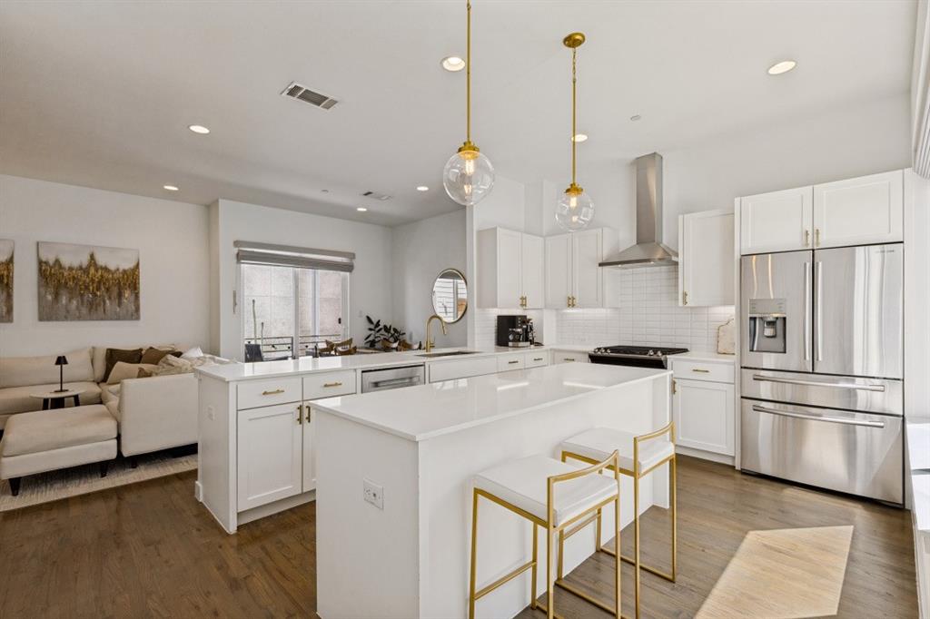 Kitchen featuring an oversized central island with quartz countertops, white shaker-style cabinetry, stainless steel appliances, and dual glass pendant lights set against wood-finish flooring