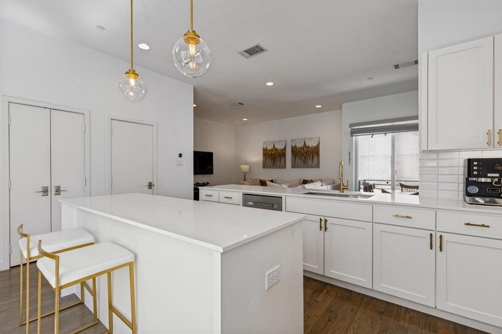 Kitchen featuring white cabinetry, quartz countertops, a subway tile backsplash, wood-finish flooring, and gold-toned hardware