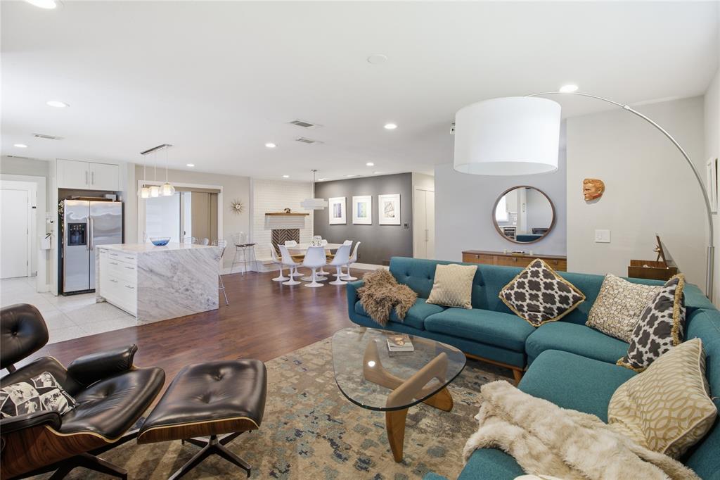 Designed for both everyday living and entertaining, the open-concept floor plan seamlessly connects the living room, dining area, and kitchen. A striking waterfall-edge kitchen island provides a natural gathering place, while the wood-burning fireplace with gas starter adds architectural character to the dining area. Rich, warm-toned flooring unifies the spaces, complemented by contemporary finishes and mid-century modern influences. The thoughtful layout provides an easy flow between cooking, dining, and relaxing while maintaining a sense of connection throughout the main living areas.