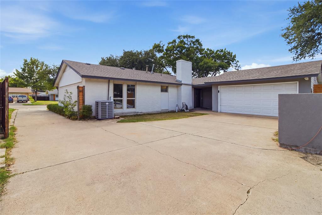 A view back toward the home reveals the attached two-car garage, with convenient interior access through the utility room. The expansive paved area provides easy maneuverability, while the home's rear-facing windows bring natural light into the living spaces. The combination of practical design and generous outdoor space makes this property as functional for everyday living as it is for entertaining.
