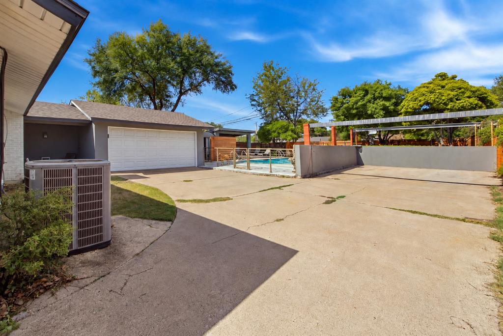 The expansive paved parking area provides additional space for vehicles beyond the attached two-car garage. Conveniently located at the end of the gated driveway, this versatile area offers flexibility for everyday parking and visiting guests. Decorative metal fencing separates the adjacent swimming pool and cabana area, helping define the property's distinct outdoor spaces.