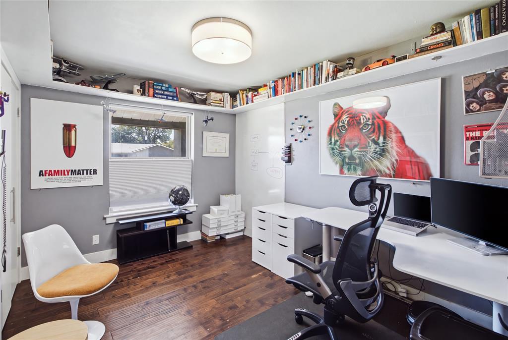 Currently arranged as a home office, this secondary bedroom demonstrates the home's flexible living spaces. Rich flooring, contemporary lighting, and extensive upper-wall shelving create a distinctive workspace, while a large window brings in natural light. The room can easily serve as a traditional bedroom, study, or creative retreat to suit your needs.