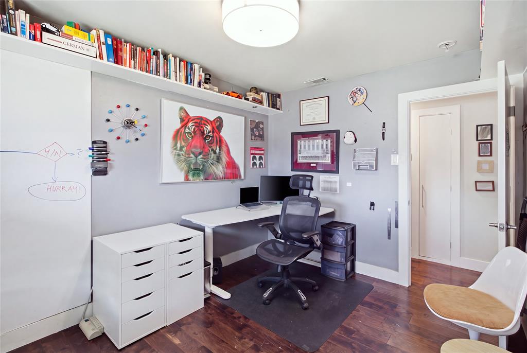 This view of the secondary bedroom, currently configured as a home office, highlights the dedicated workspace, extensive overhead shelving, and rich, warm-toned flooring. The flexible layout offers options for working from home, pursuing hobbies, or returning the space to traditional bedroom use.