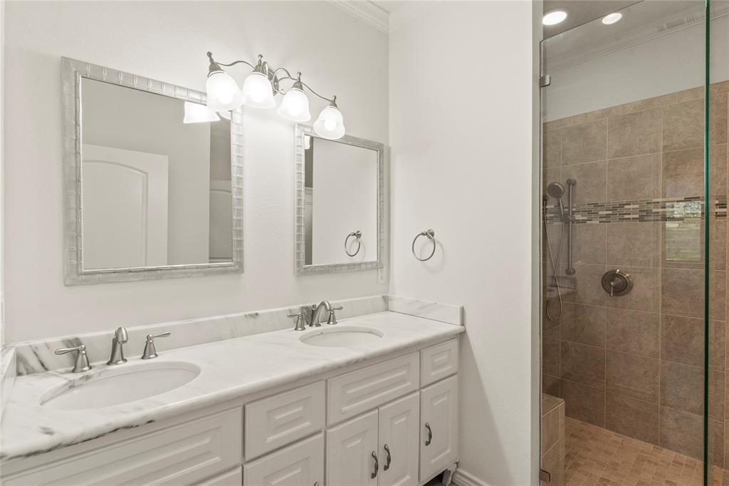 Primary bathroom featuring a double-sink vanity with marble-look countertops and a large walk-in tiled shower.