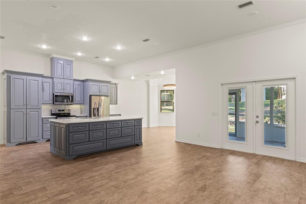 Open-concept living and kitchen area with high ceilings, a large center island, and French doors leading to the screened porch.