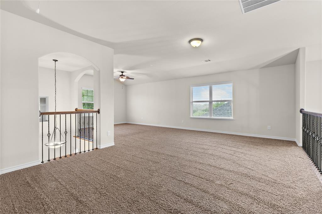 Expansive open-concept space featuring vaulted ceilings, neutral wall tones, carpeted flooring, wrought-iron staircase railing, and a decorative arched entryway