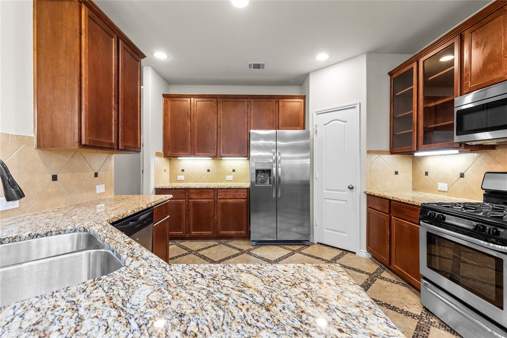 Kitchen featuring natural wood cabinetry, stone-finish countertops, stainless steel appliances, a tile backsplash with decorative accents, and tile flooring with diamond-pattern detailing