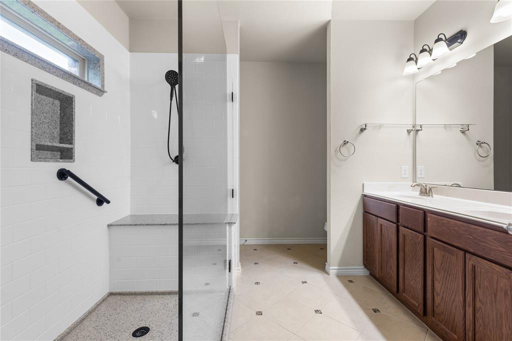 Walk-in shower with a glass enclosure, built-in stone-top bench, and matte black hardware, paired with a wood-finish dual-sink vanity and tiled flooring