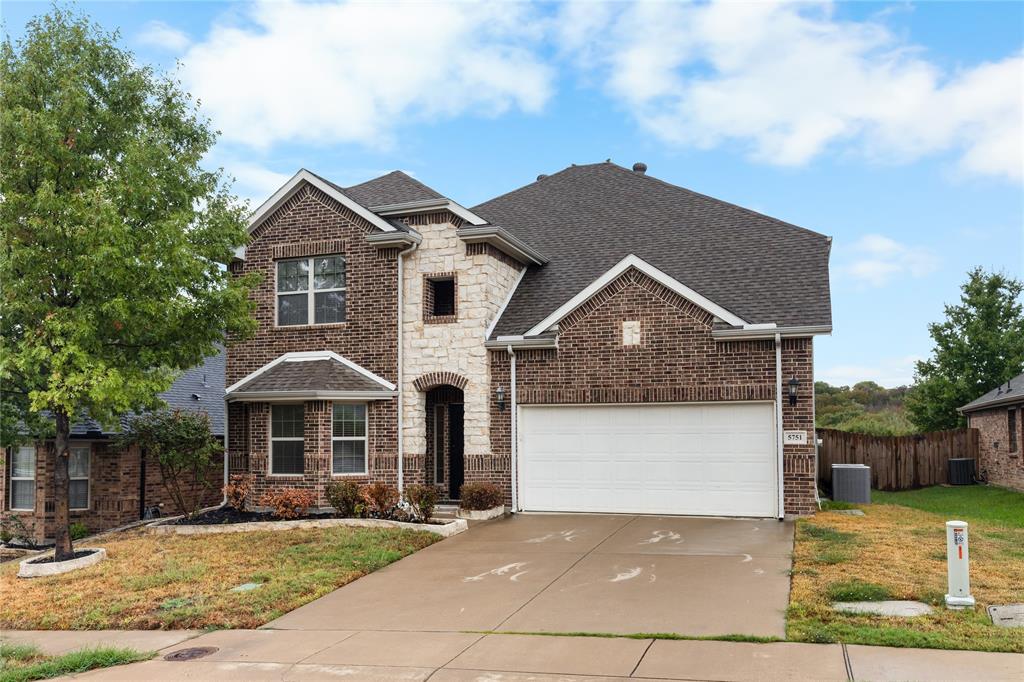 Two-story exterior featuring a brick and stone facade, a multi-gabled roofline, and an attached two-car garage with a concrete driveway