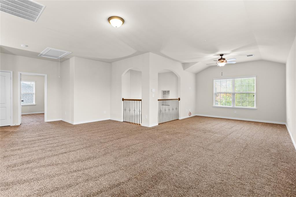 Expansive carpeted room featuring vaulted ceilings, arched entryways, metal spindle railings, and an integrated ceiling fan with lighting