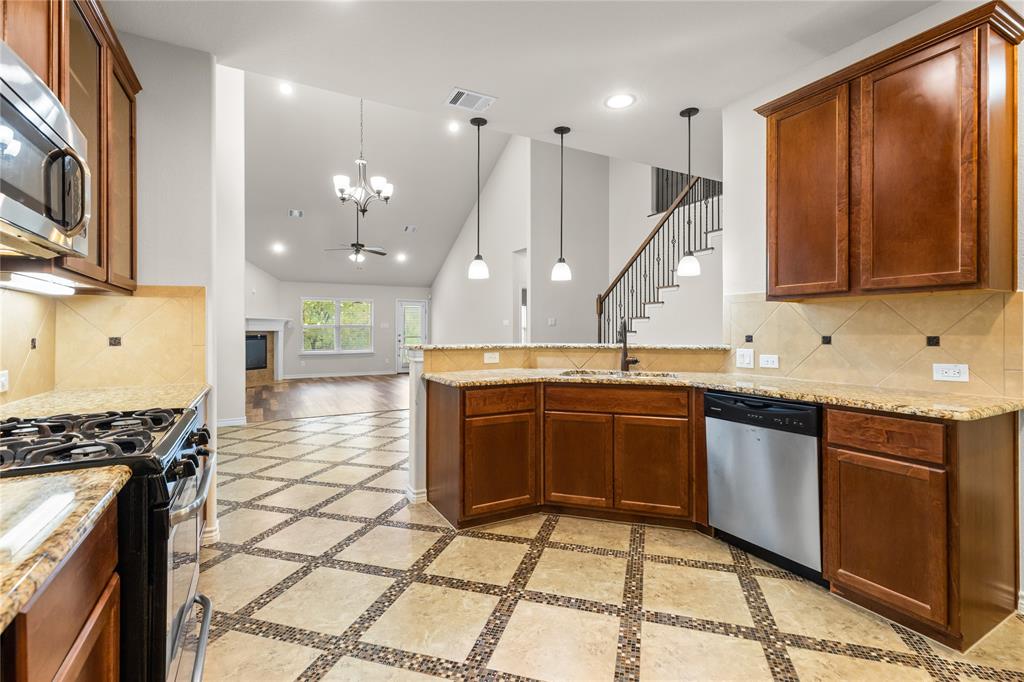 Kitchen featuring stained wood cabinetry, stone-patterned countertops, geometric-patterned tile flooring, stainless steel appliances, and triple pendant lighting