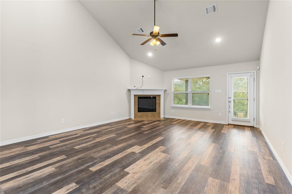 Vaulted ceiling featuring a central ceiling fan, wood-finish flooring, and a fireplace with a mantel and tiled surround