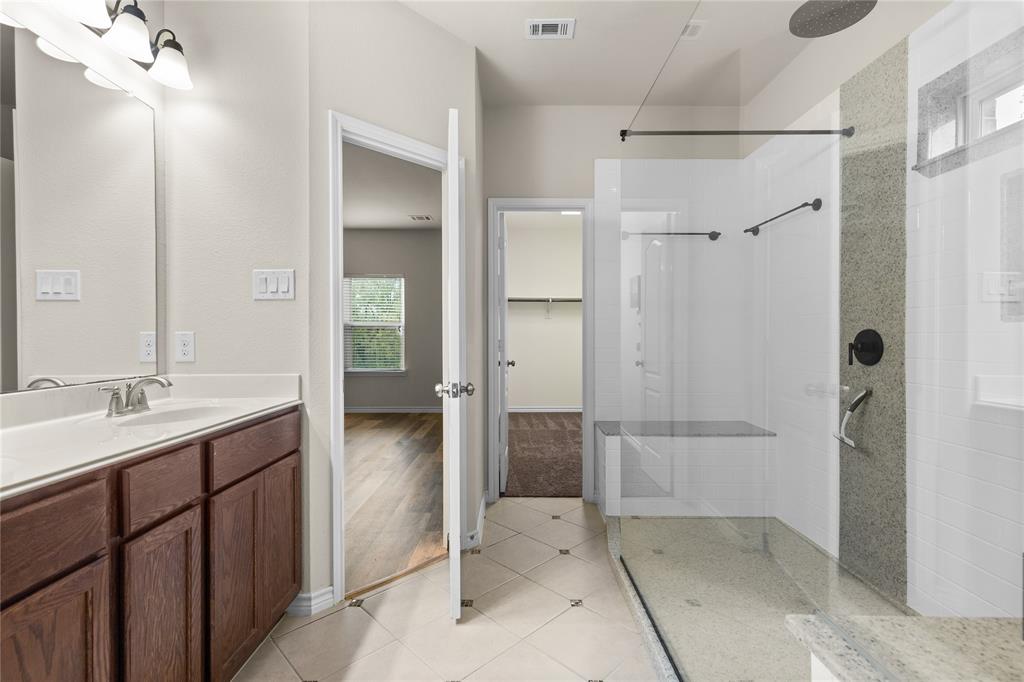 Bathroom featuring a vanity with wood-finish cabinetry, a white countertop with an integrated sink, and a walk-in shower with a glass enclosure, a stone-tile accent wall, and a built-in bench
