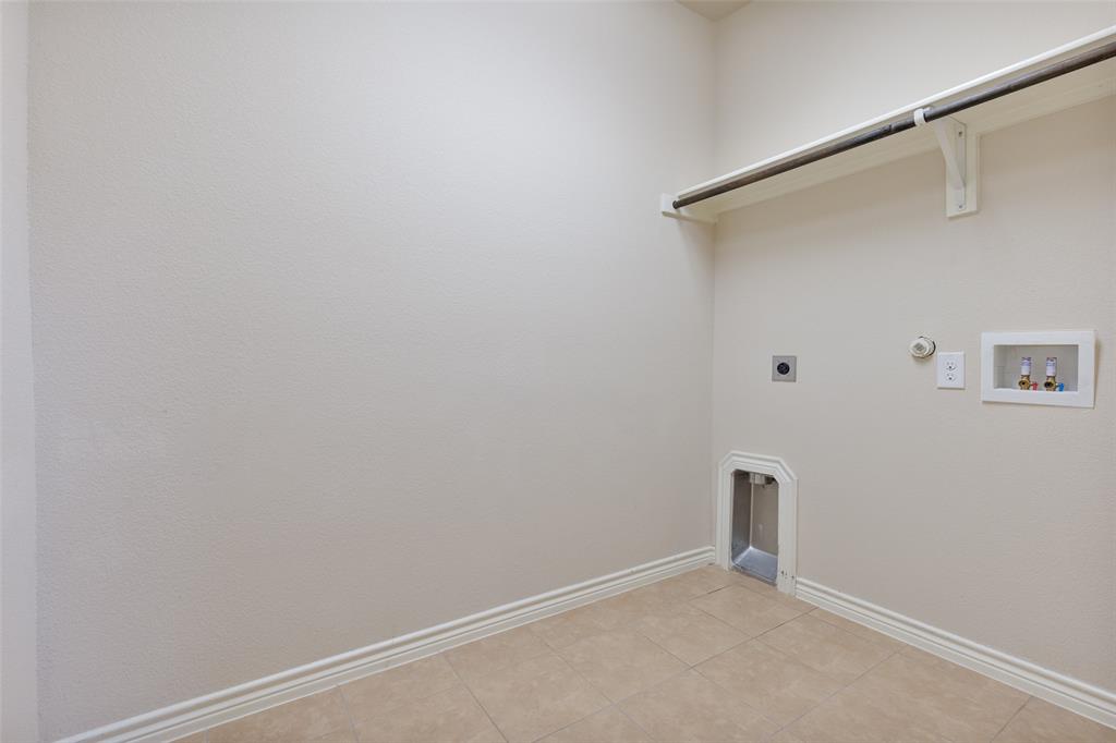 Dedicated utility space featuring tile flooring, neutral wall finishes, integrated shelving, and dedicated plumbing connections