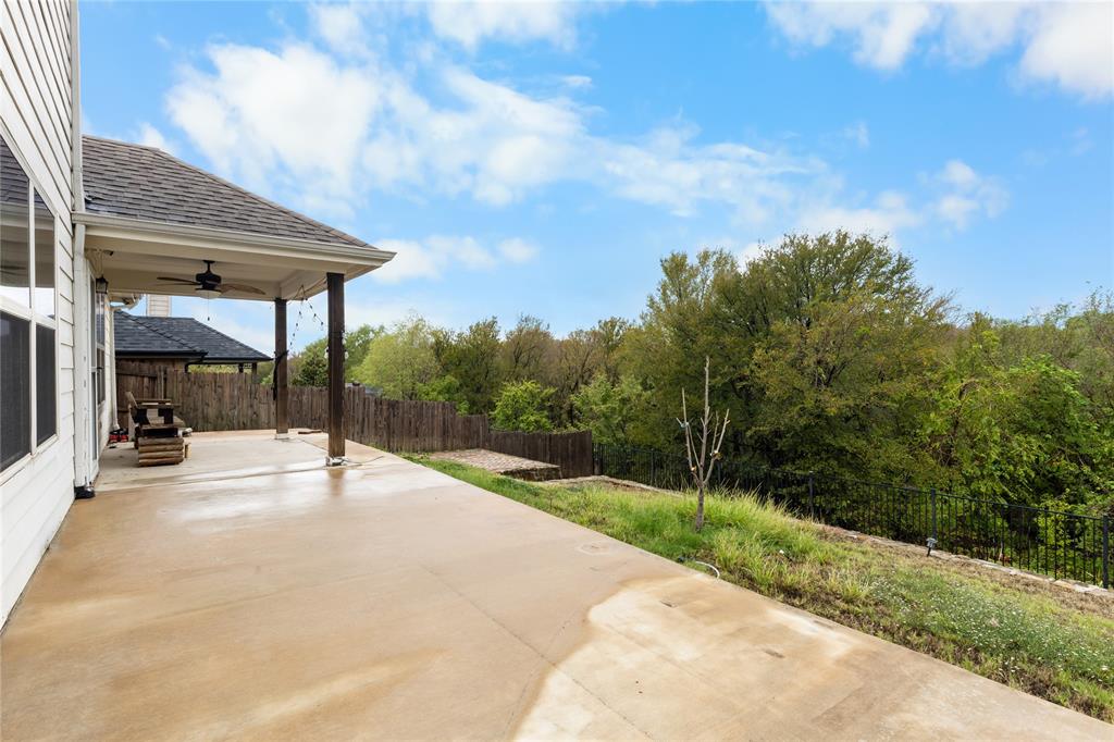 Covered concrete patio featuring a ceiling-mounted fan and an open backyard with wood fencing and mature trees