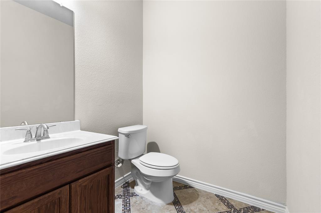 Bathroom featuring a wood-finish vanity with a light-toned countertop, integrated oval sink, chrome-finish widespread faucet, and decorative tile flooring with mosaic accents