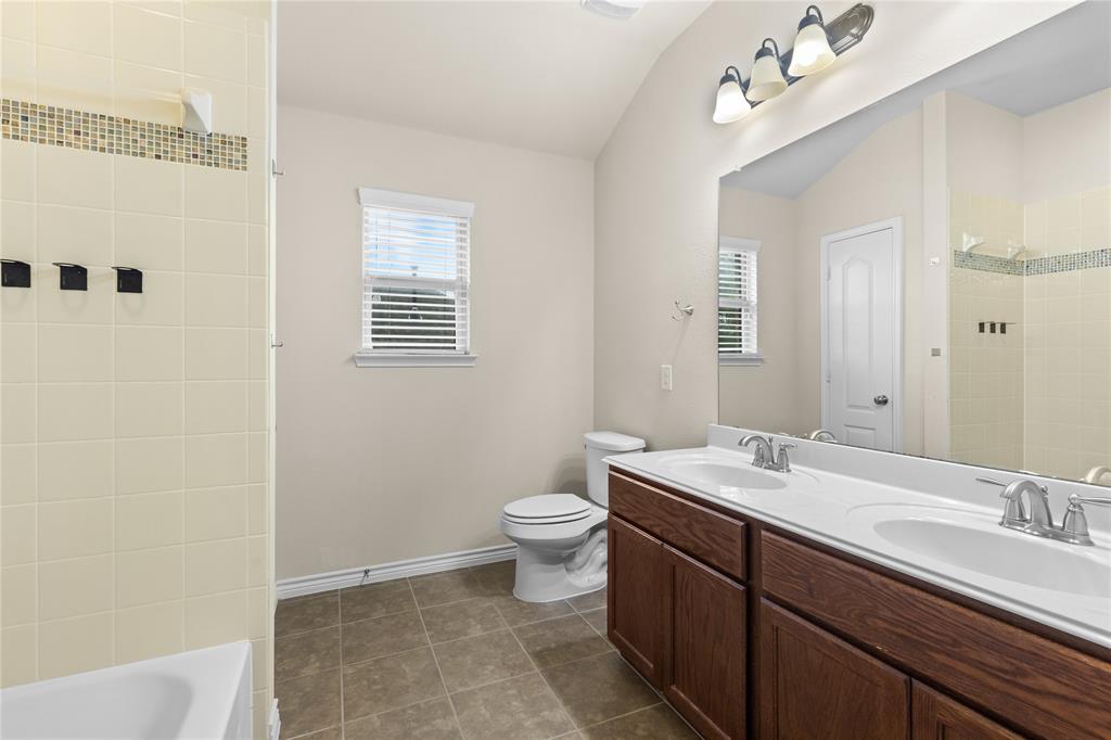 Bathroom featuring a double vanity with integrated sinks, large wall-mounted mirror, ceramic tile flooring, and a shower-tub combination with tiled surround