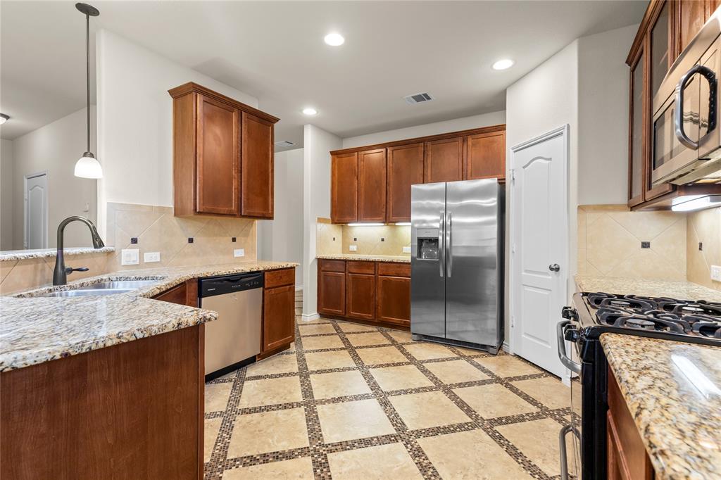 Kitchen featuring wooden cabinetry, stone-surface countertops, tile backsplash with decorative accents, stainless steel appliances, and tile flooring with a geometric inlay pattern
