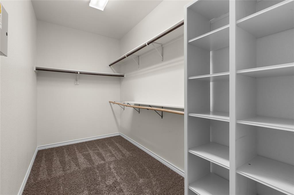 Storage area featuring built-in floor-to-ceiling shelving, multiple tiers of hanging rods, and neutral carpeting
