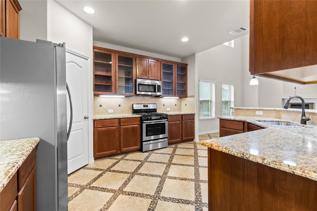 Kitchen featuring warm-toned wood cabinetry with glass-front uppers, stone-patterned countertops, stainless steel appliances, and tile flooring with decorative mosaic inlay