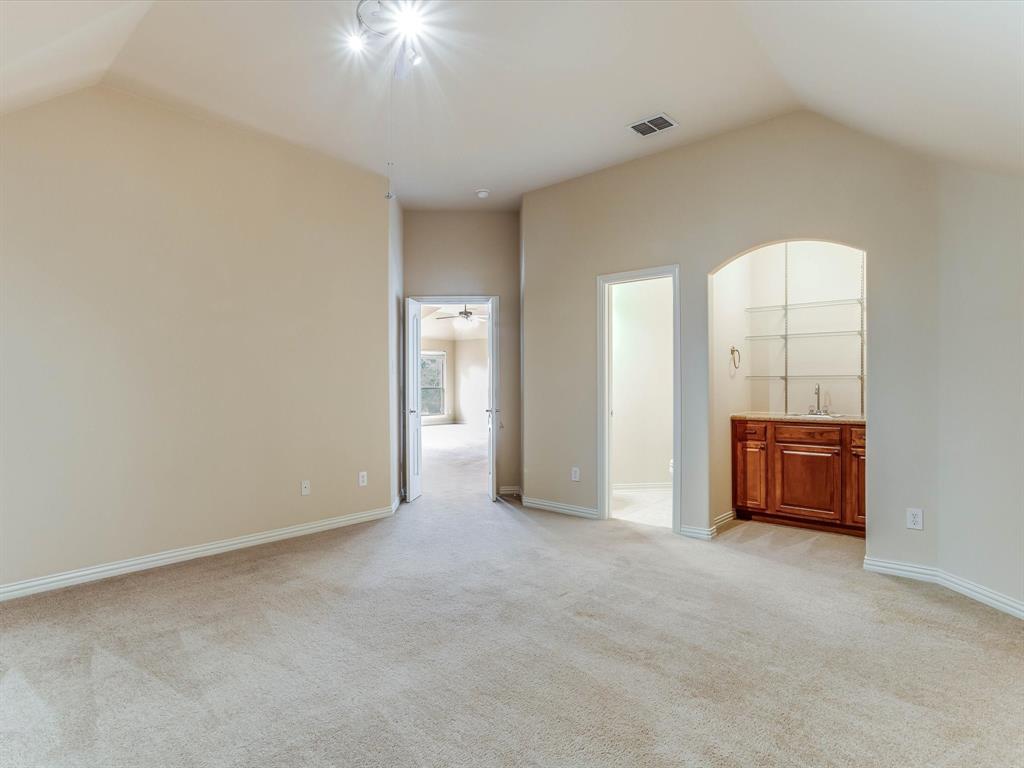 Vaulted ceilings, carpeted flooring, and a built-in wet bar featuring wood cabinetry, a sink, and glass shelving