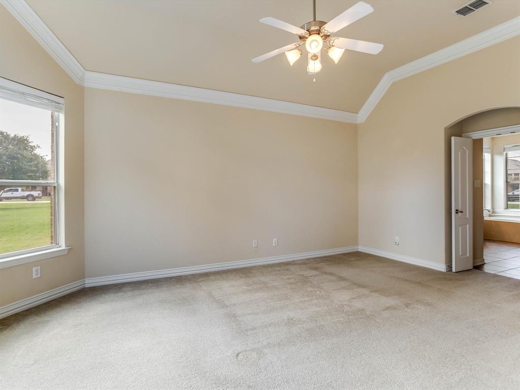 Vaulted ceiling featuring crown molding, neutral carpeting, a central ceiling fan with multi-light fixture, and an arched doorway entry