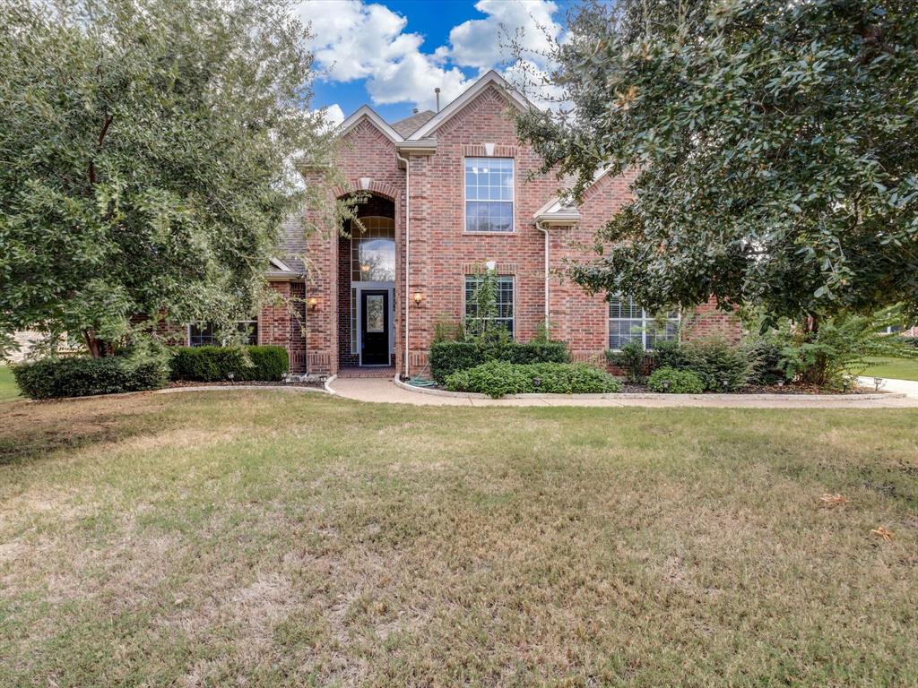 Multi-level brick exterior featuring a steeply pitched roofline, arched entryway, multi-pane windows, and mature landscaping