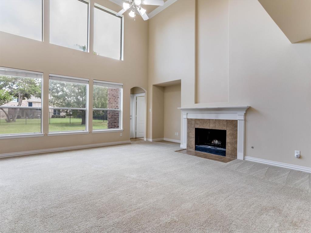 High-ceilinged room featuring expansive floor-to-ceiling windows, a fireplace with a white mantel and tile surround, and a ceiling-mounted light fixture