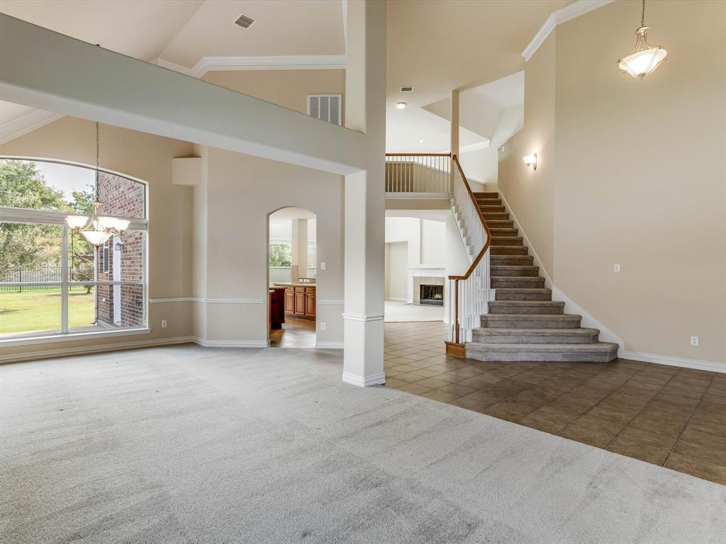 Vaulted ceilings, expansive arched windows, ceramic tile and carpeted flooring, a staircase with a wooden handrail, and built-in crown molding