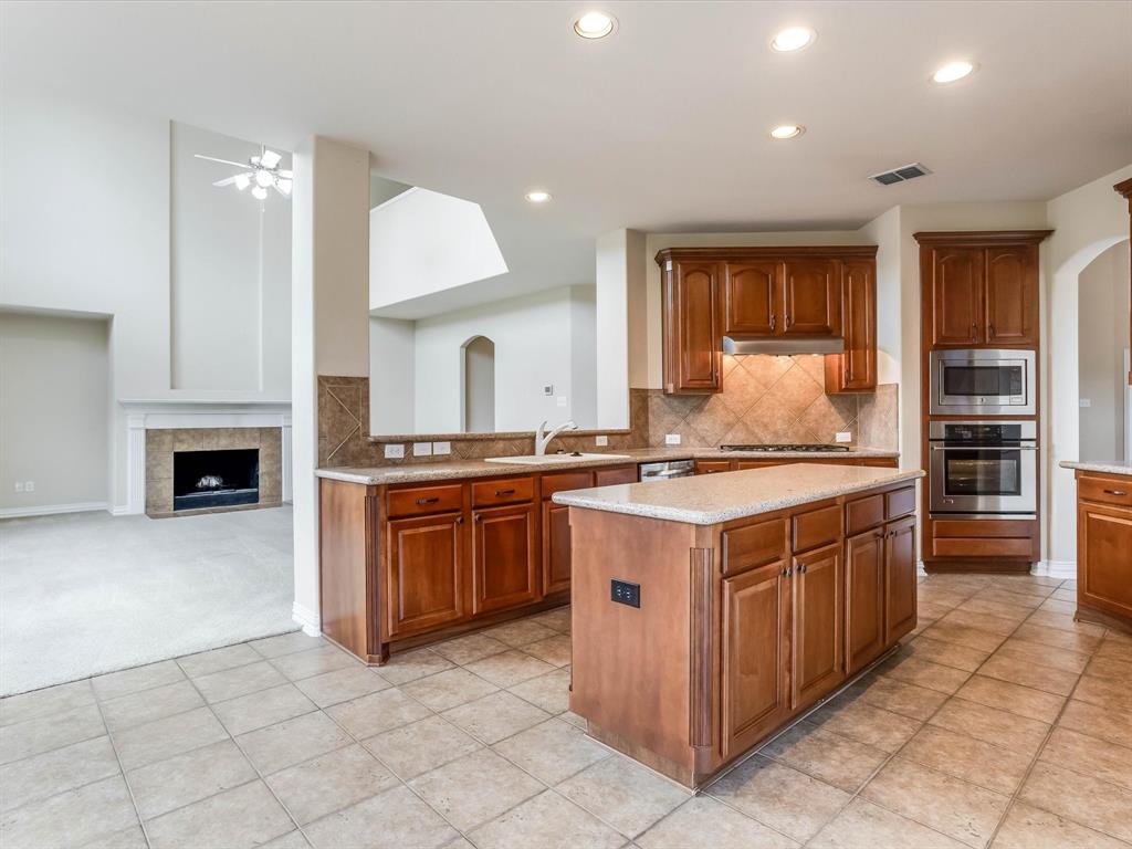 Kitchen featuring stained-wood cabinetry, stone-finish countertops, tile backsplash, built-in stainless steel appliances, and an island with under-counter storage